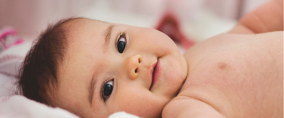 Close up of baby lying on blanket looking at camera.