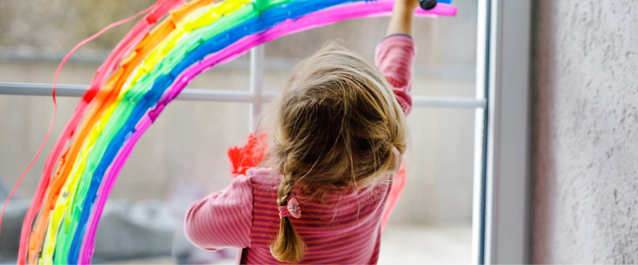 Preschool child painting a rainbow on a window.